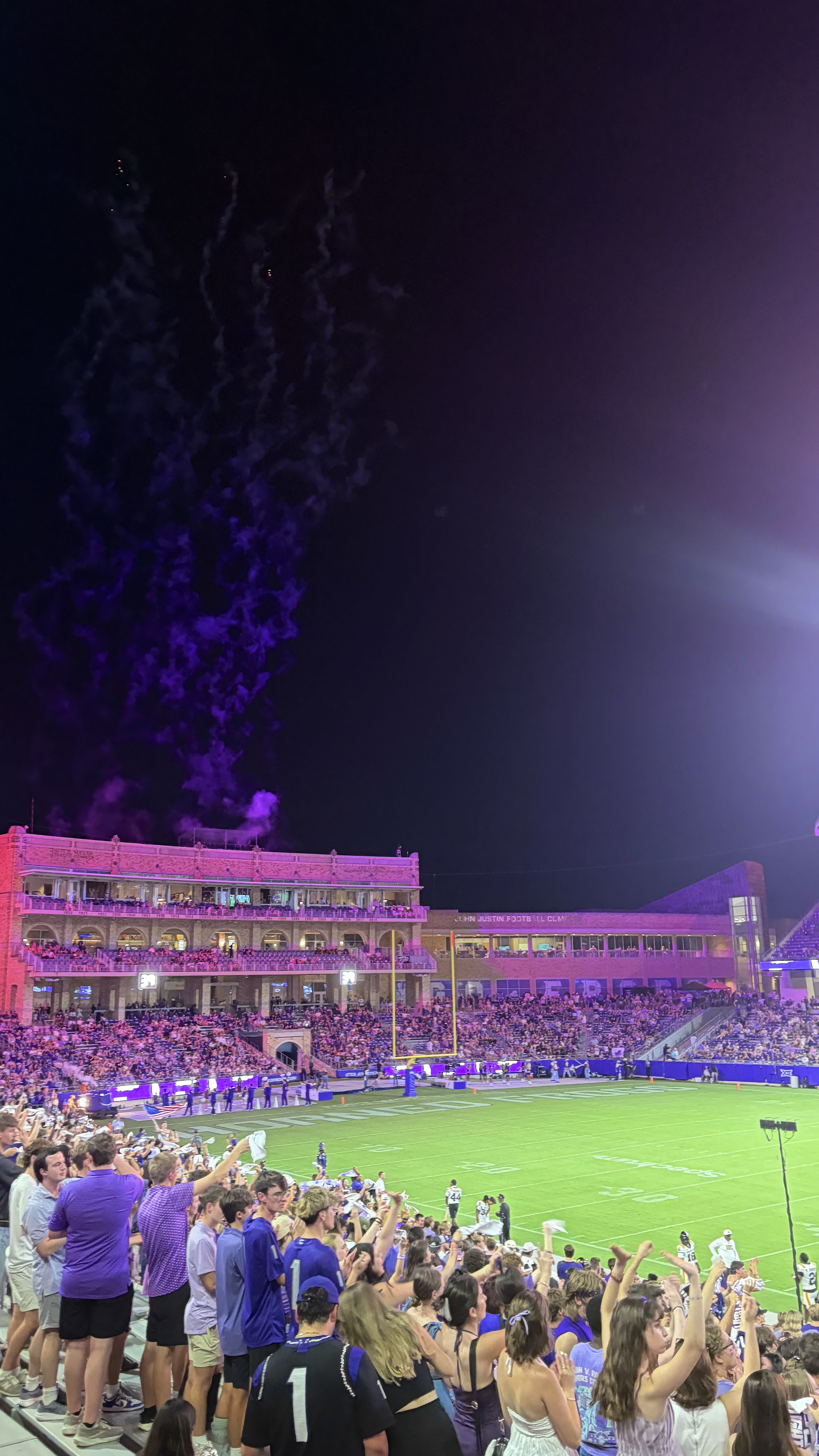 Students cheering in a college football stadium lit in purple
